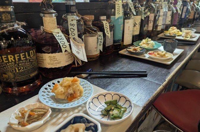 Small plates and a sake bottle set out along an izakaya counter