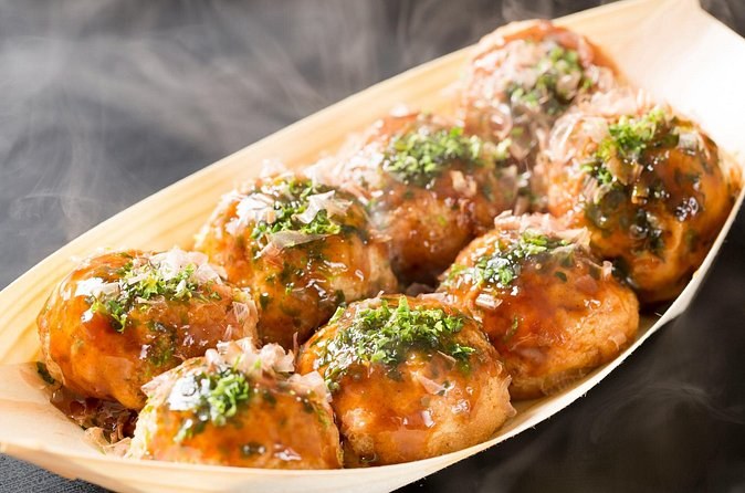 A tray of takoyaki topped with sauce and spring onion